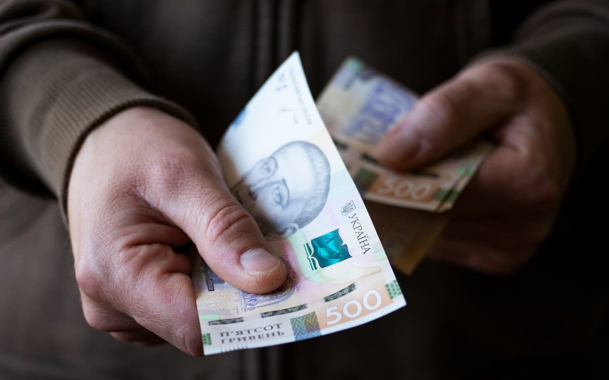 Крупним планом чоловік дає українські грошові купюри.